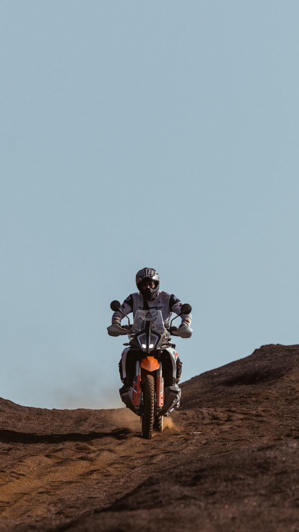 Rider on a KTM adventure bike cresting a dirt hill