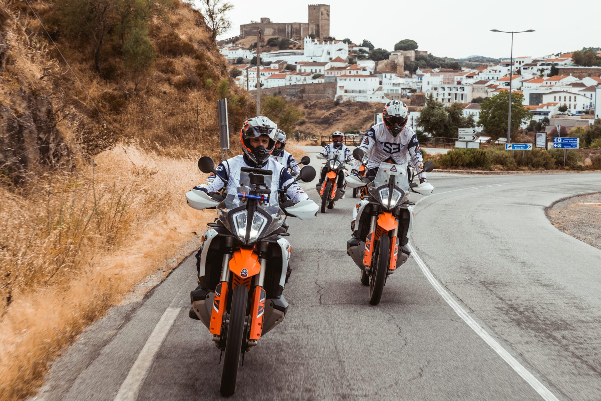 Riders on KTM adventure bikes approaching a white Andalusian village with a hilltop castle