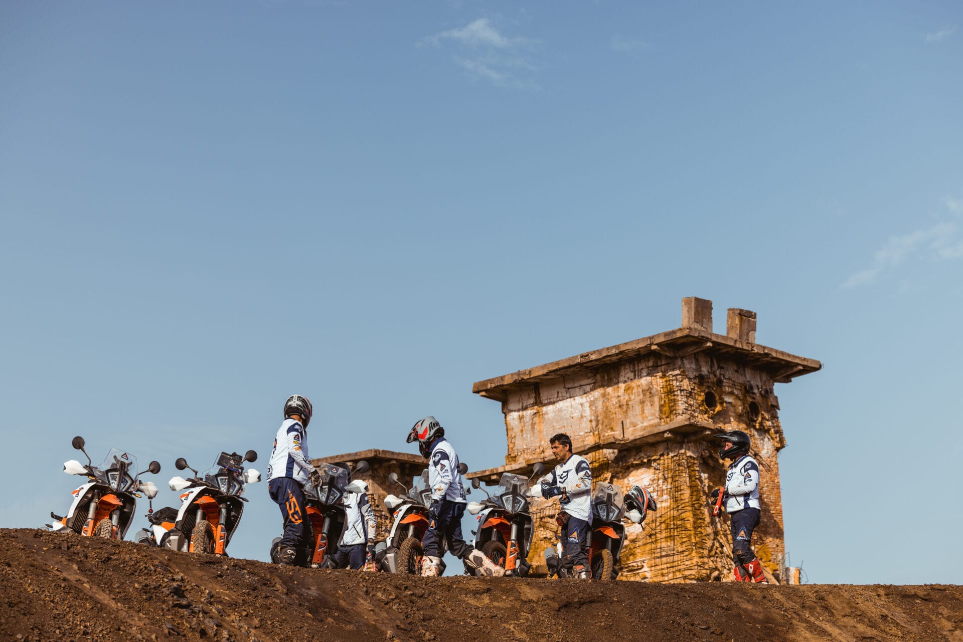 Riders standing with their KTM adventure bikes beside a stone ruin on a hilltop