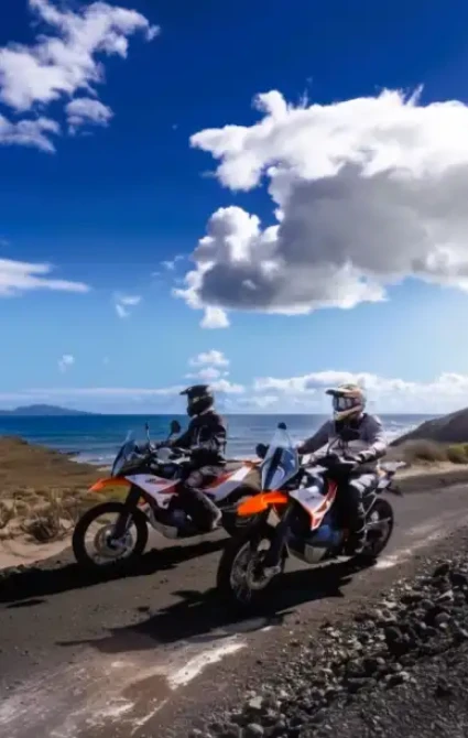 Two riders on KTM adventure bikes on a coastal road in the Canary Islands