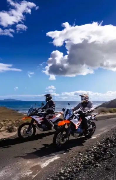 Two riders on KTM adventure bikes on a coastal road in the Canary Islands