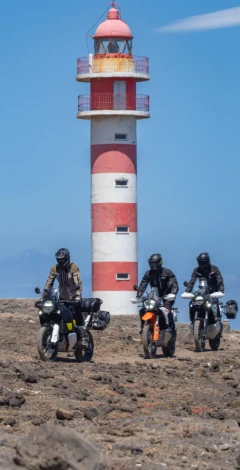 Three riders on adventure bikes beside a red and white lighthouse in the Canary Islands