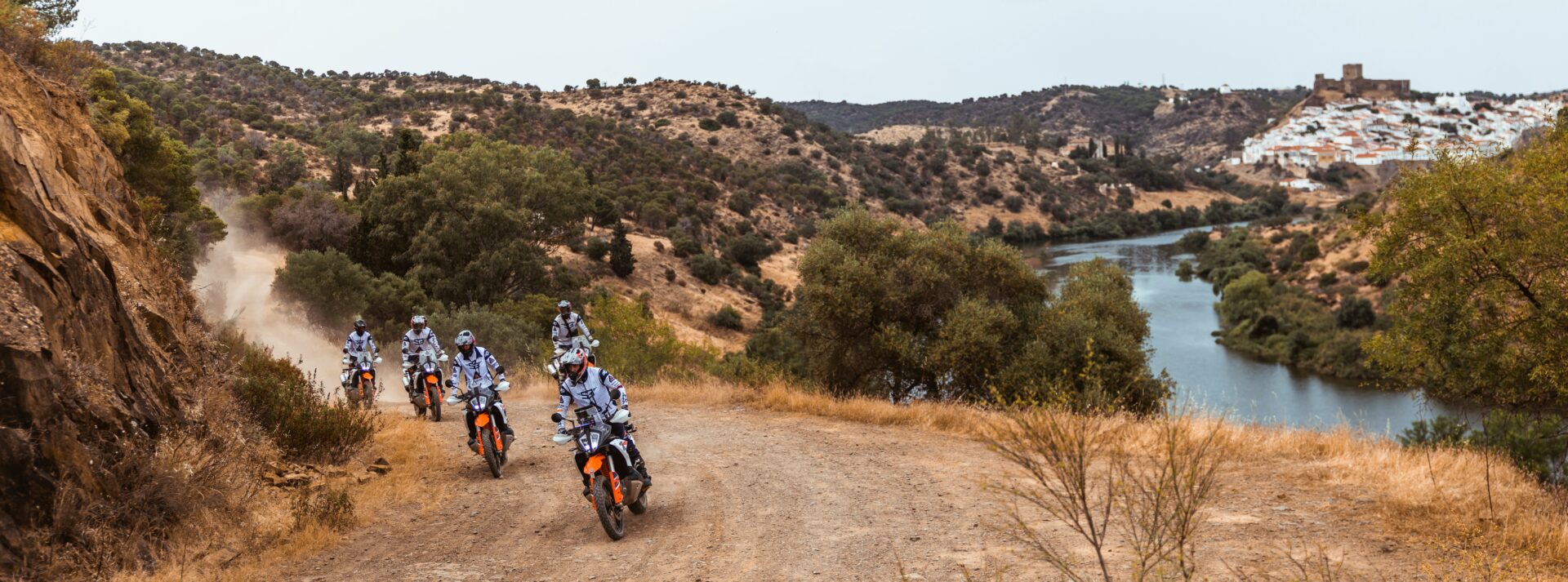 Riders on KTM adventure bikes on a dirt track above a river on the Spain and Portugal tour