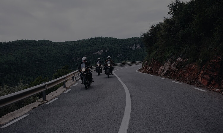 Riders on a quiet mountain road with a guardrail on an overcast day