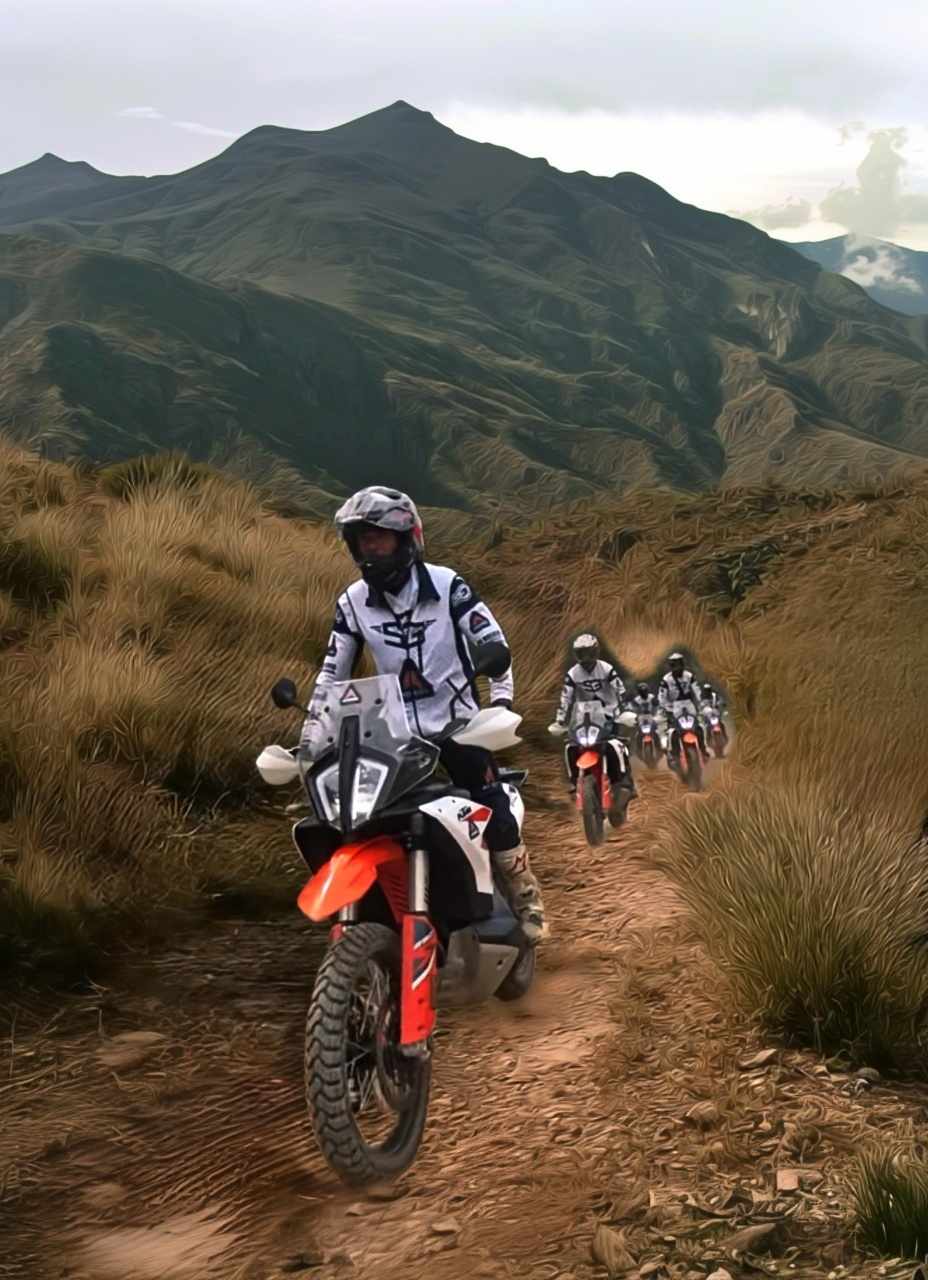 Group of riders on KTM adventure bikes on a dirt track through mountain grassland