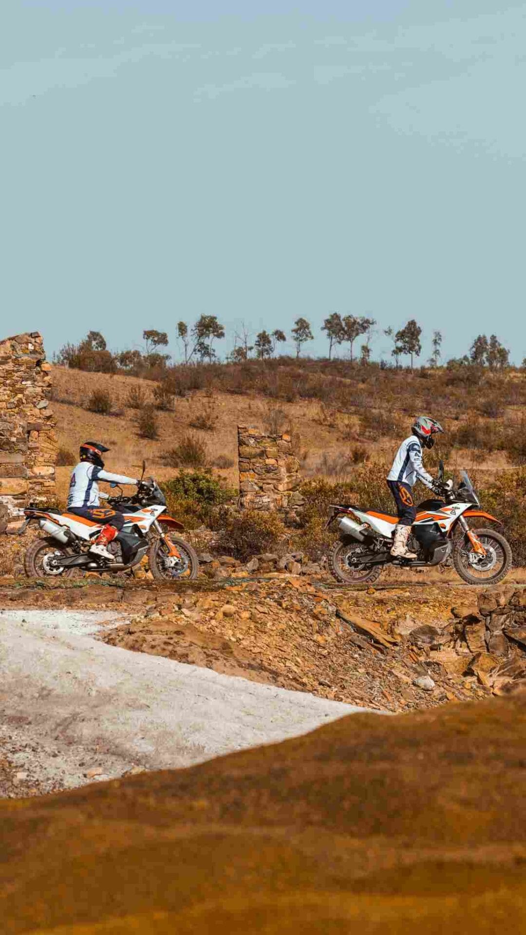 Two riders on KTM adventure bikes on a red earth hillside