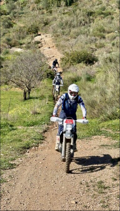 Enduro riders on a narrow singletrack climbing a green hillside near Granada