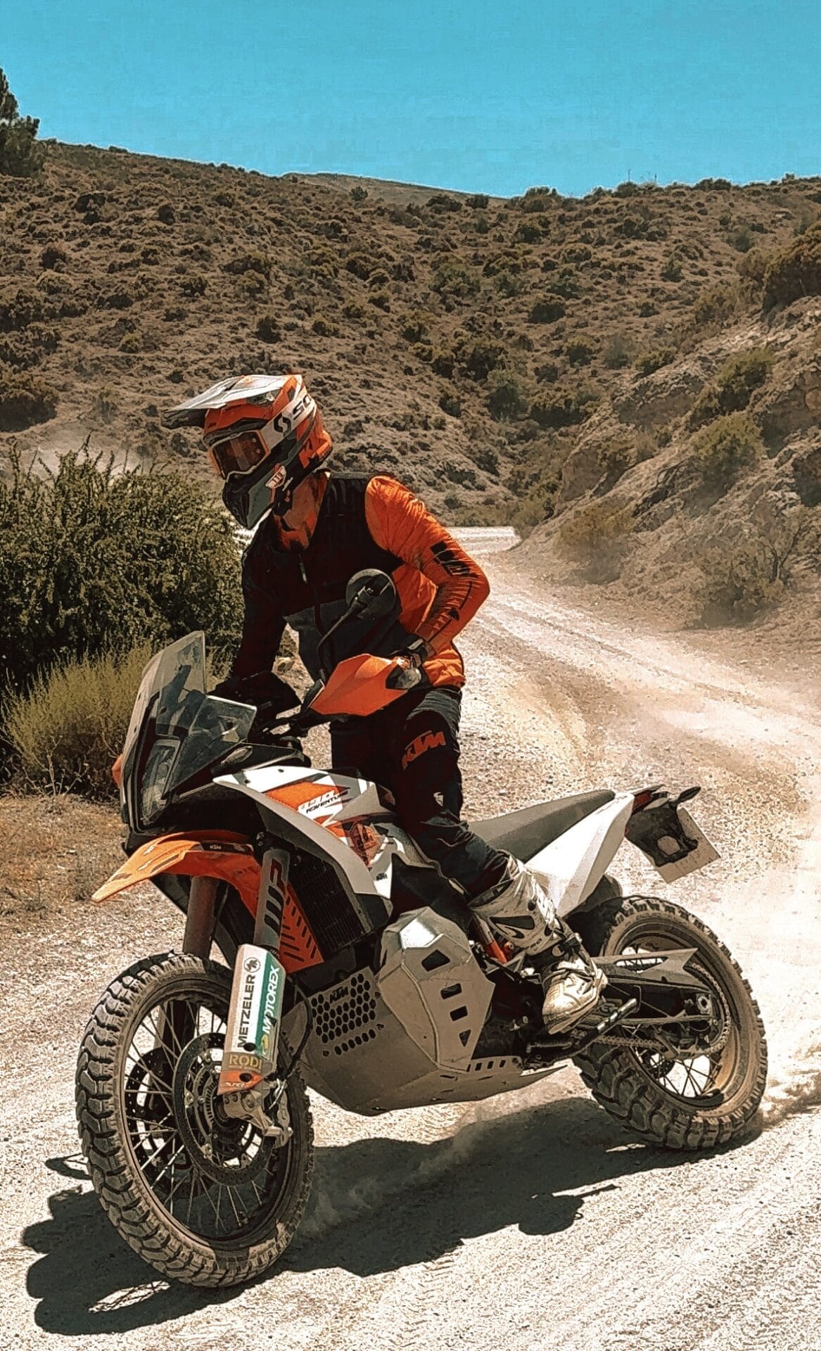 Rider standing on the pegs of a KTM adventure bike on a gravel track