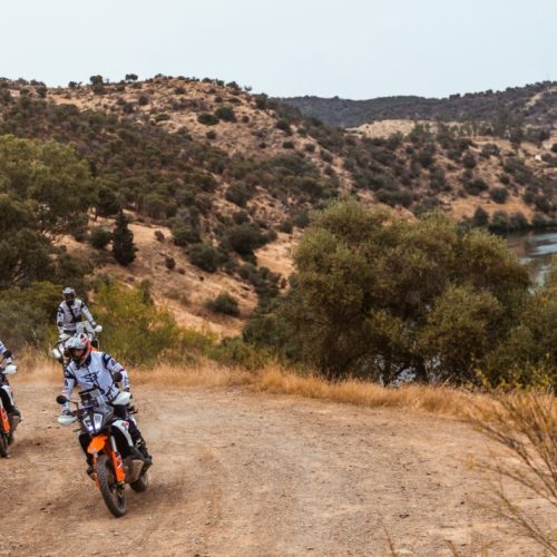 Riders on KTM adventure bikes on a dirt track above a river on the Spain and Portugal tour