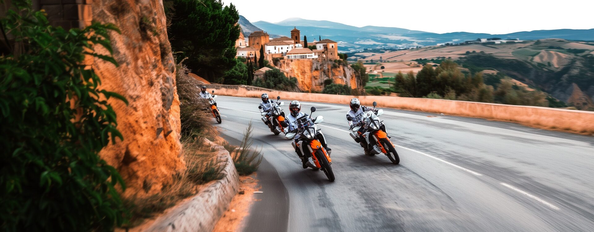 Group of riders on KTM adventure bikes on a winding road below a hilltop village in Andalusia