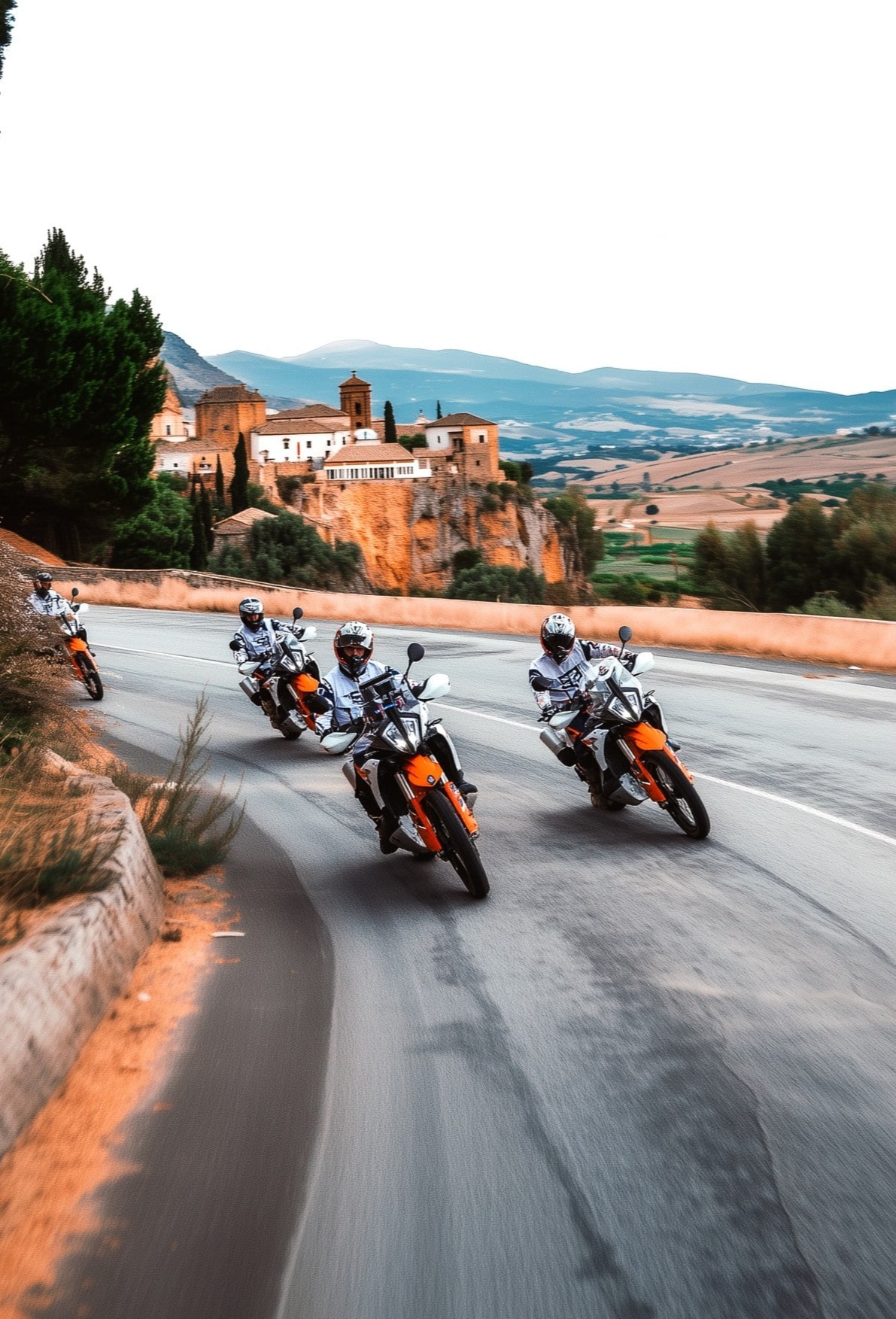 Riders on KTM adventure bikes on a winding asphalt road below a hilltop village