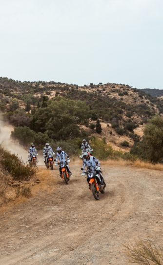 Group of riders on KTM adventure bikes on a dusty track through scrubby hills