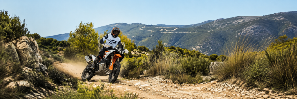 Rider on a KTM adventure bike on a dirt track through Mediterranean hills