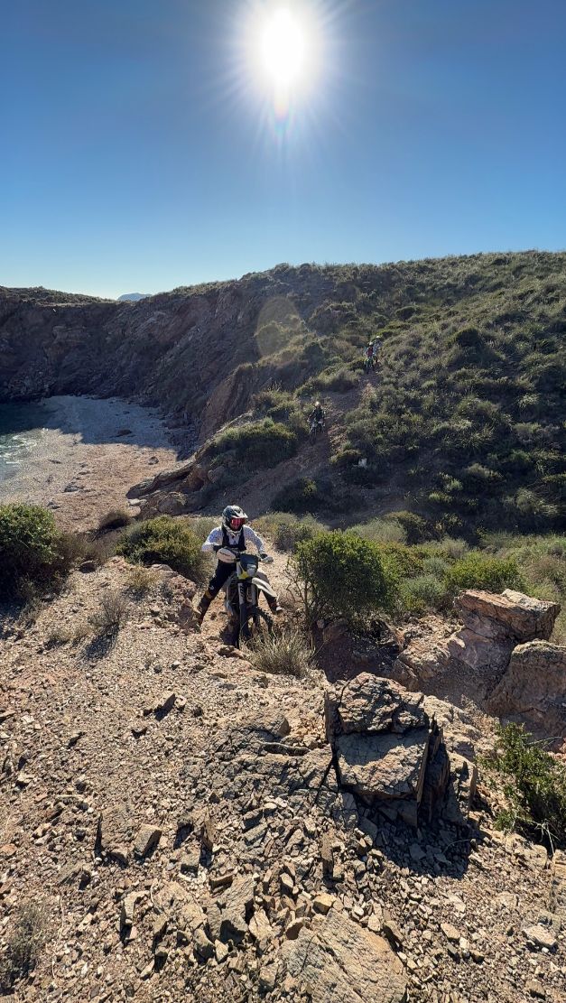 Enduro rider climbing a rocky slope above a coastal ravine