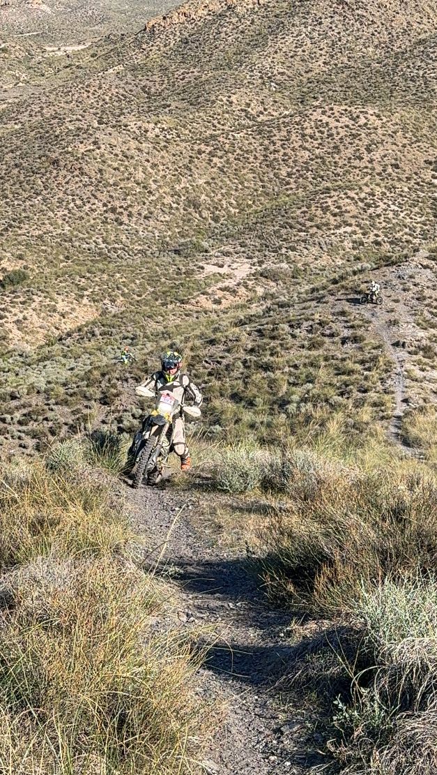 Enduro rider coming up a singletrack on a dry grassy hillside