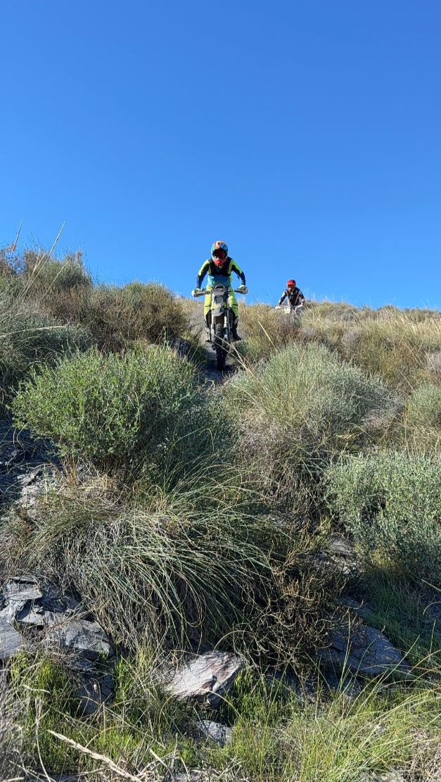 Enduro rider coming down a steep grassy ridge towards the camera