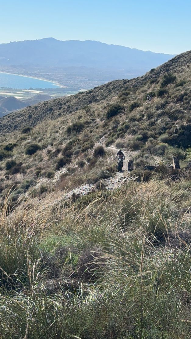 Enduro riders crossing a steep mountainside above the Mediterranean coast