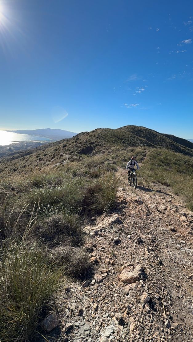 Enduro rider climbing a rocky ridge trail with the sea in the distance