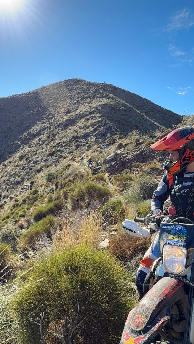 Enduro rider pausing below a mountain summit on a ridge trail