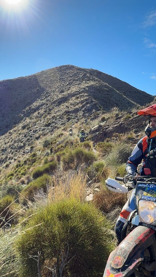 Enduro rider on a ridge trail below a sunlit mountain peak