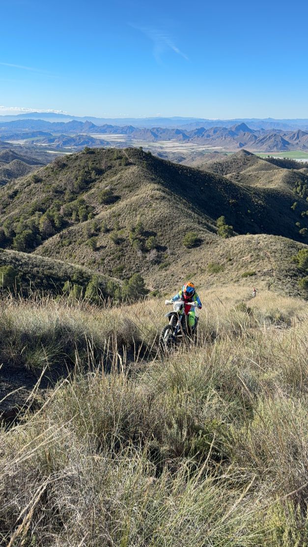 Enduro rider climbing a grassy slope with mountain views in Murcia