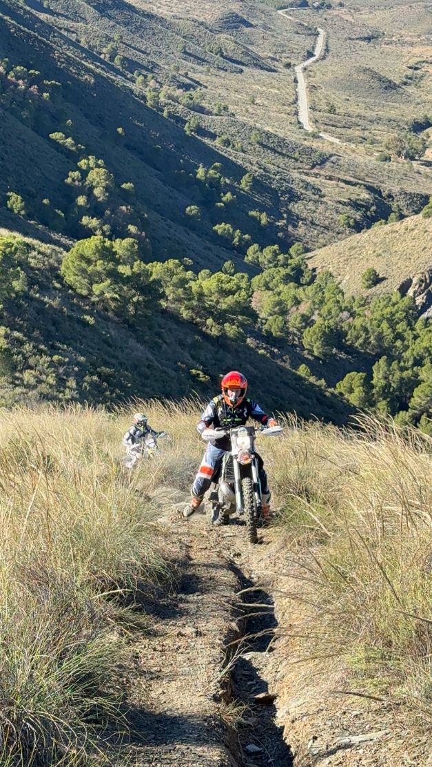 Enduro riders following a rutted singletrack through tall grass