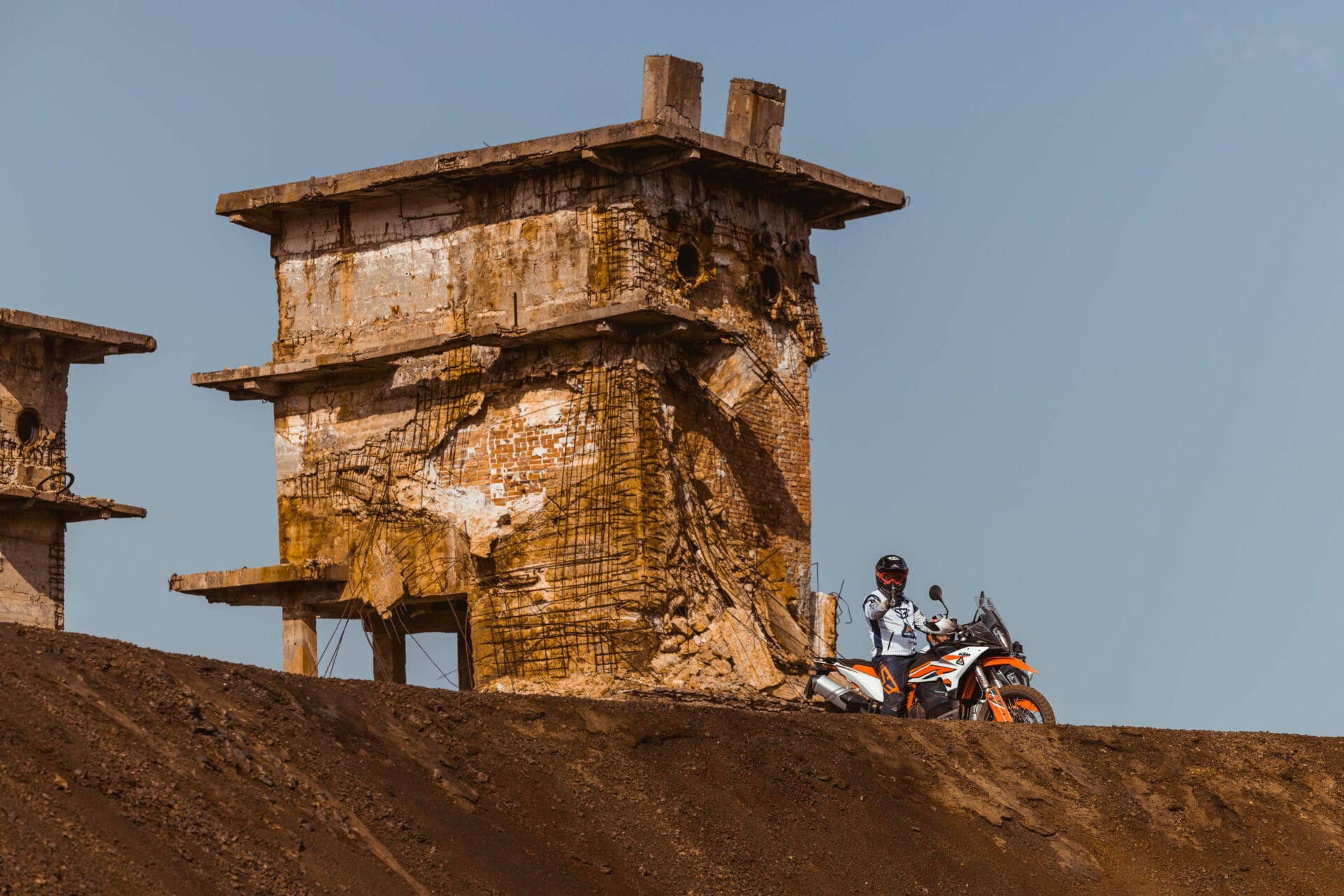 Rider on a KTM adventure bike beside an abandoned stone ruin on a hilltop