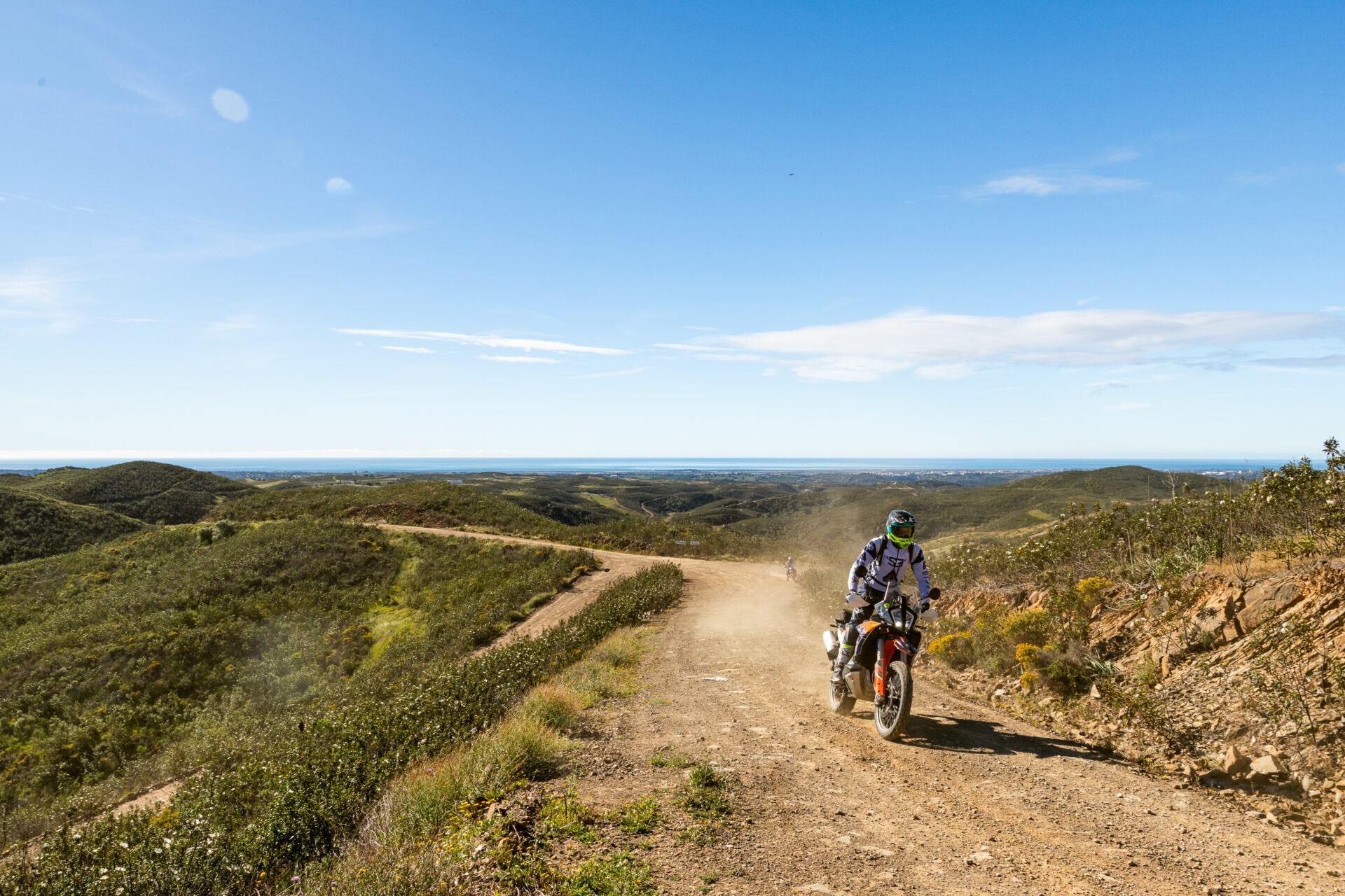 Rider on a KTM adventure bike on a dusty hill track with the ocean on the horizon in Portugal