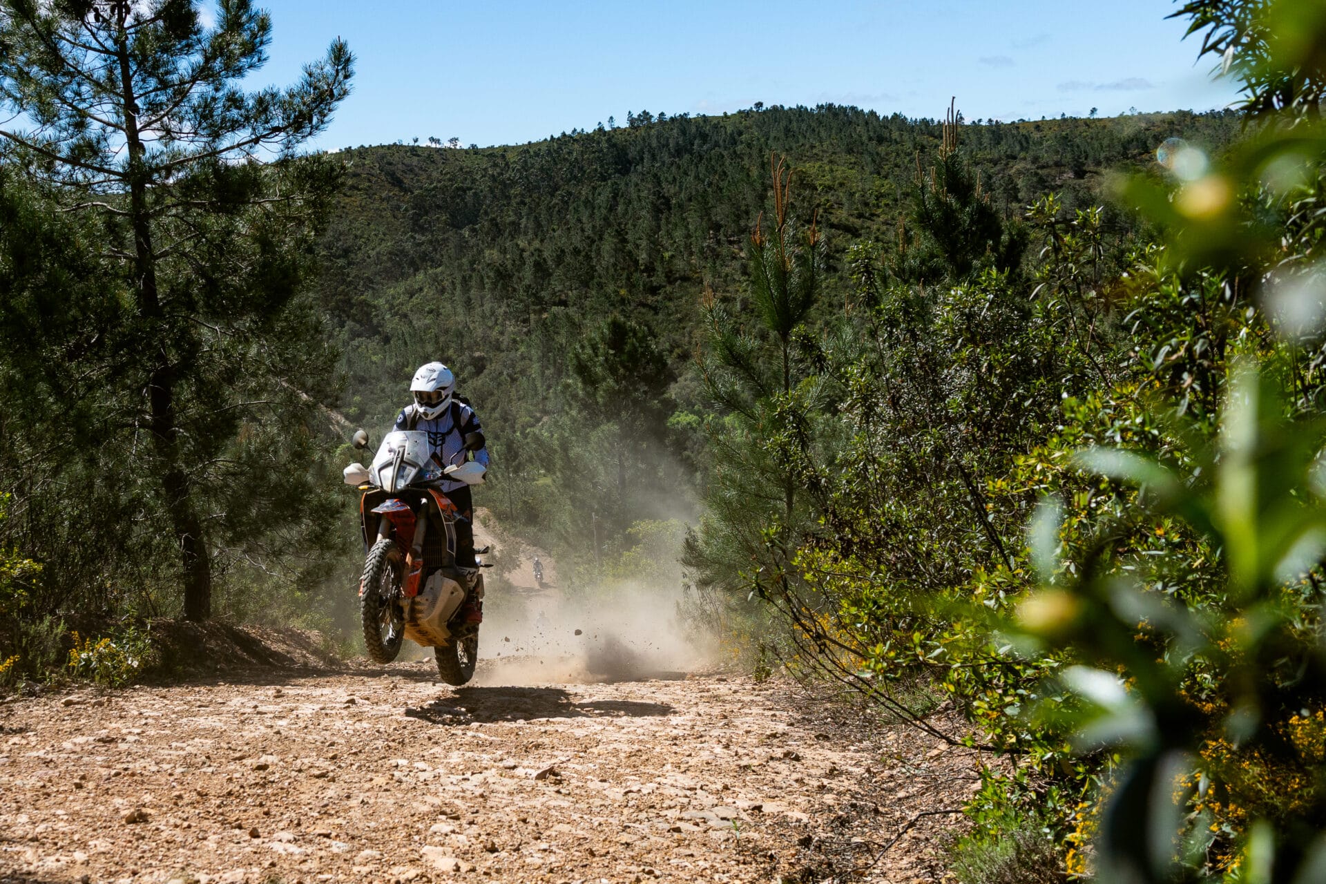 Rider on a KTM adventure bike raising dust on a gravel forest track in Portugal