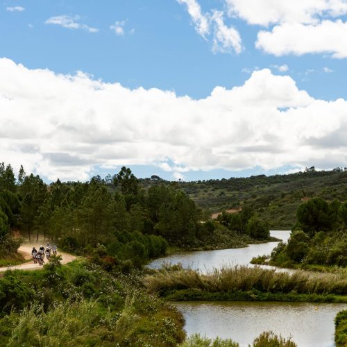 Riders on a track beside a winding river in the green hills of Portugal