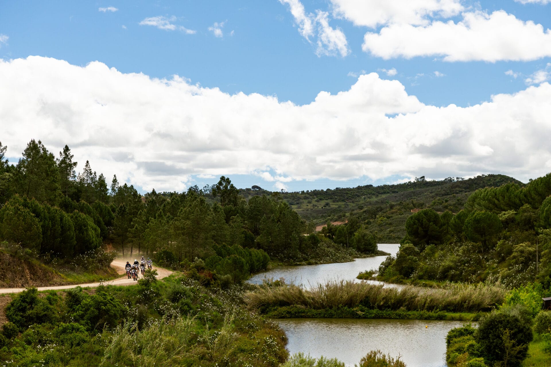 Riders on a track beside a winding river in the green hills of Portugal