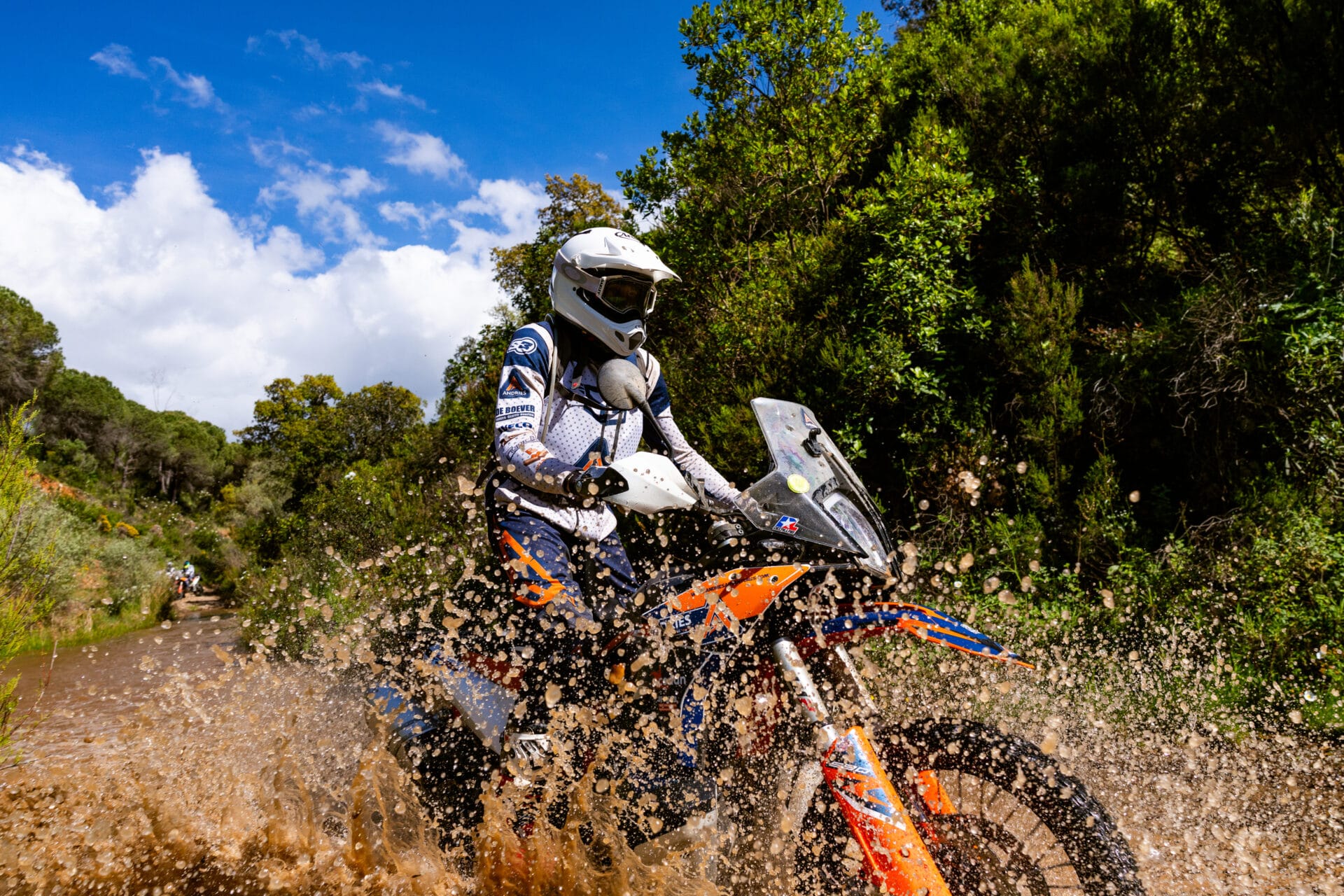 Rider on a KTM adventure bike splashing through a stream crossing in Portugal