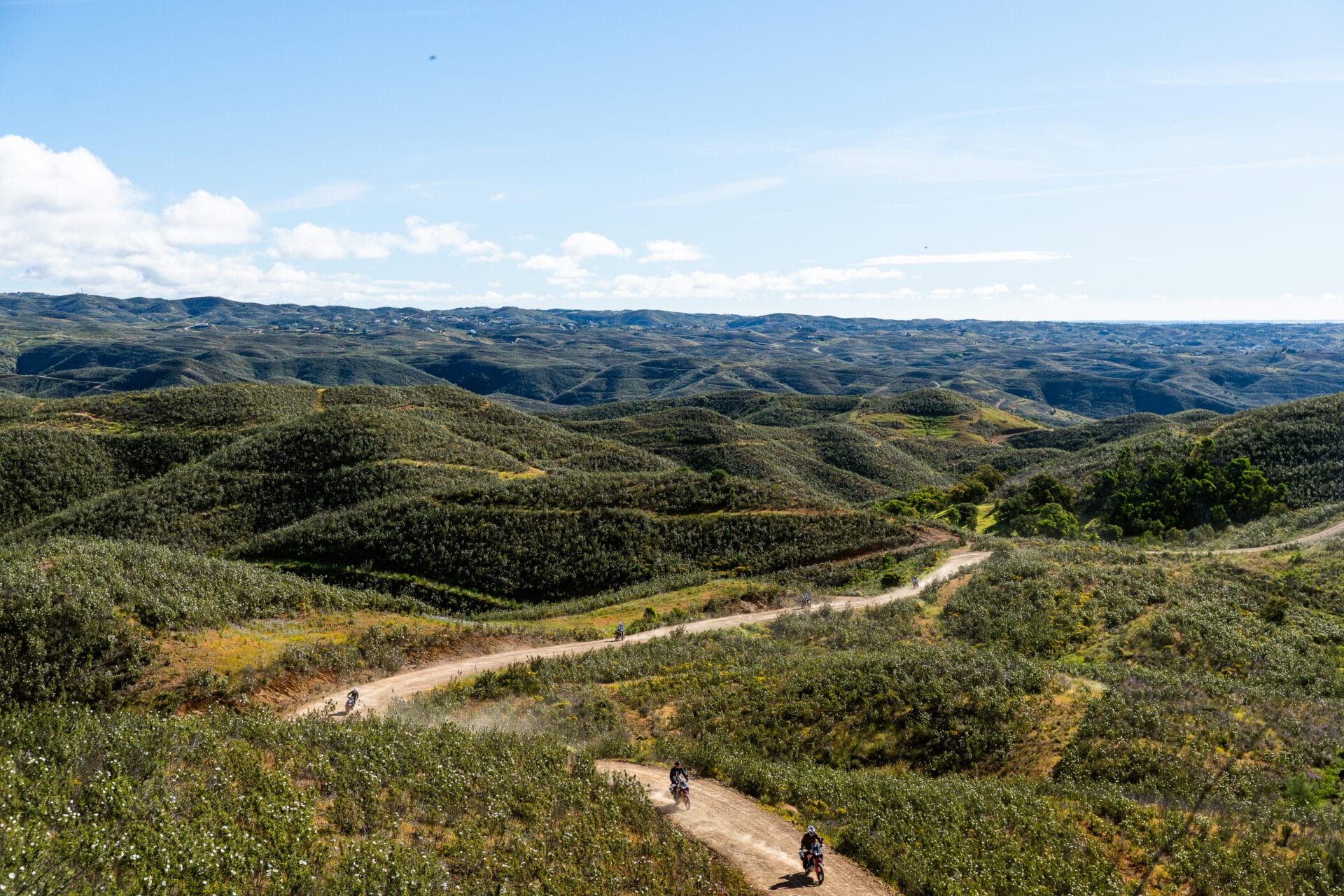 Riders on a dirt track winding through rolling green hills in Portugal