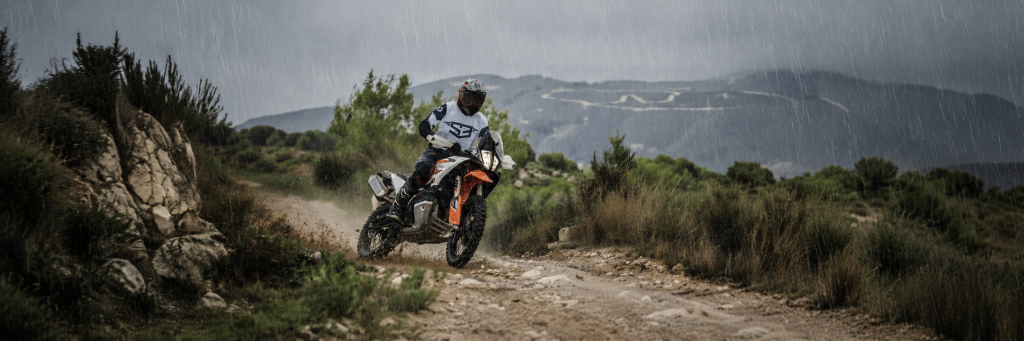 Rider on a KTM adventure bike on a dirt track under dark rain clouds