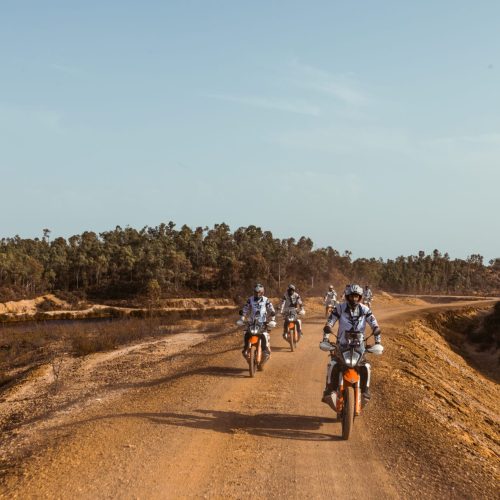 Riders on KTM adventure bikes on a sandy track through dry scrubland on the Almuñécar to Tavira tour