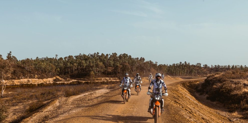 Riders on KTM adventure bikes on a sandy track through dry scrubland on the Almuñécar to Tavira tour
