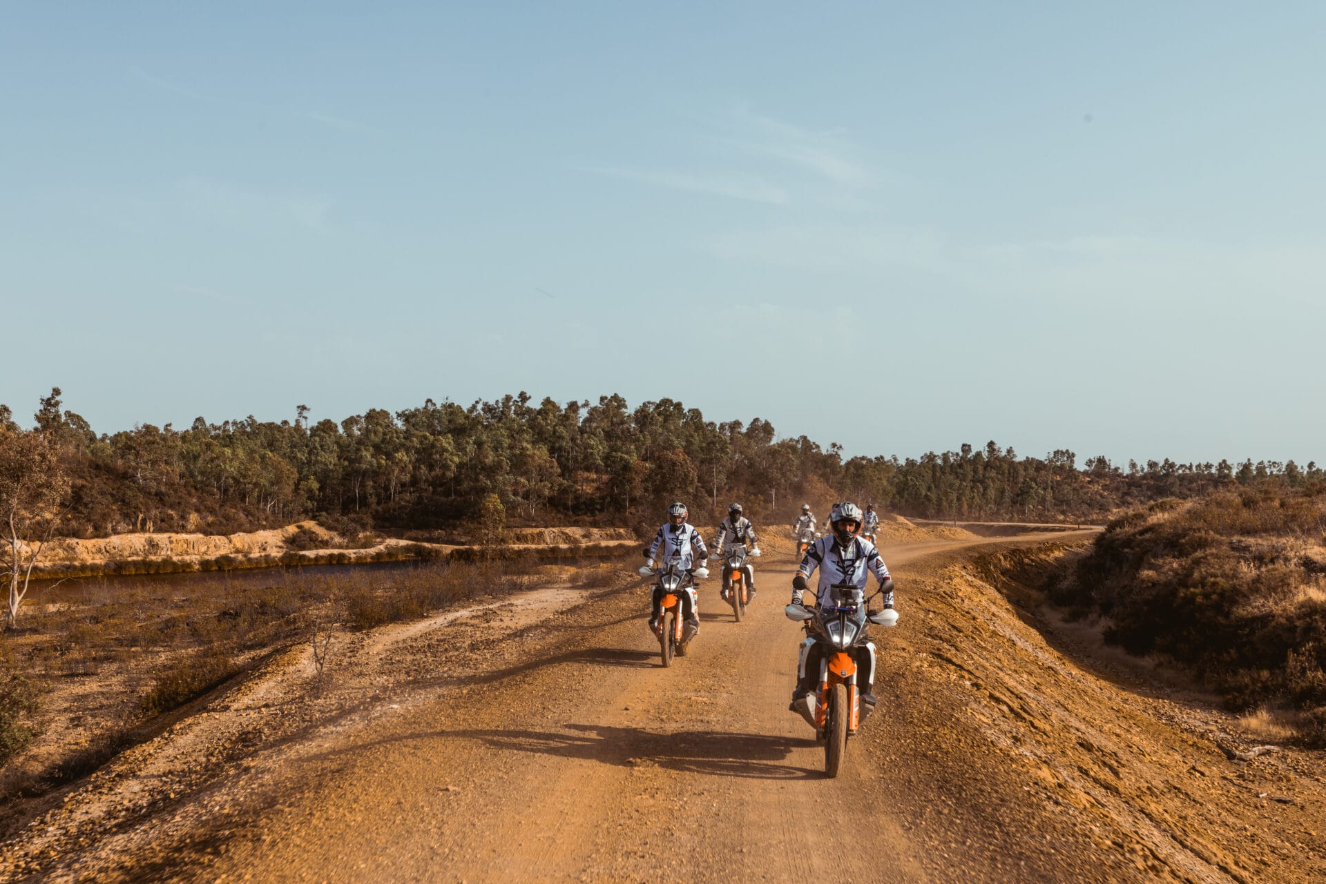 Riders on KTM adventure bikes on a sandy track through dry scrubland on the Almuñécar to Tavira tour