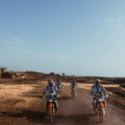 Riders on KTM adventure bikes crossing a dusty track past old ruins on the Tavira to Almuñécar tour