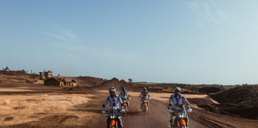 Riders on KTM adventure bikes crossing a dusty track past old ruins on the Tavira to Almuñécar tour