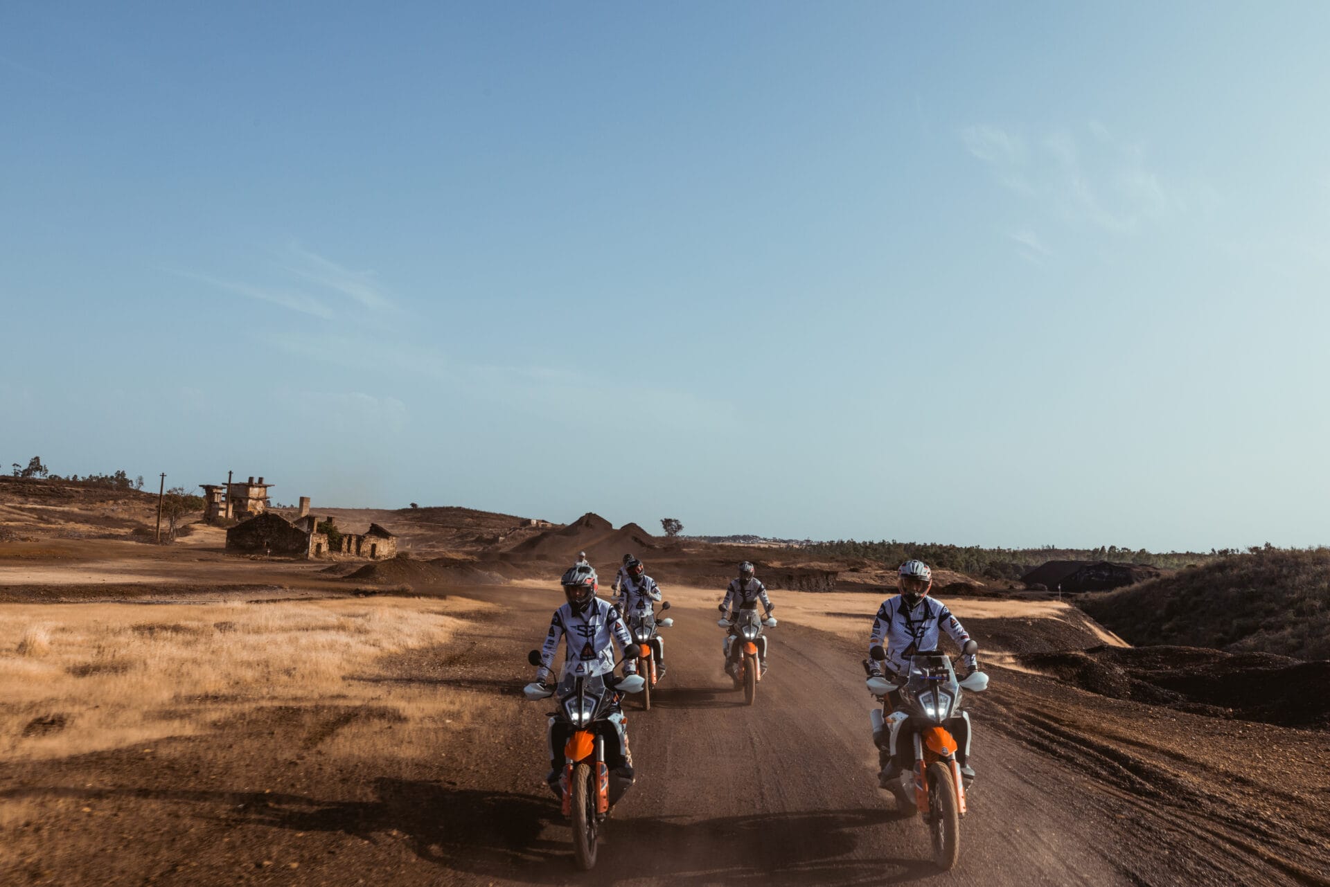 Riders on KTM adventure bikes crossing a dusty track past old ruins on the Tavira to Almuñécar tour
