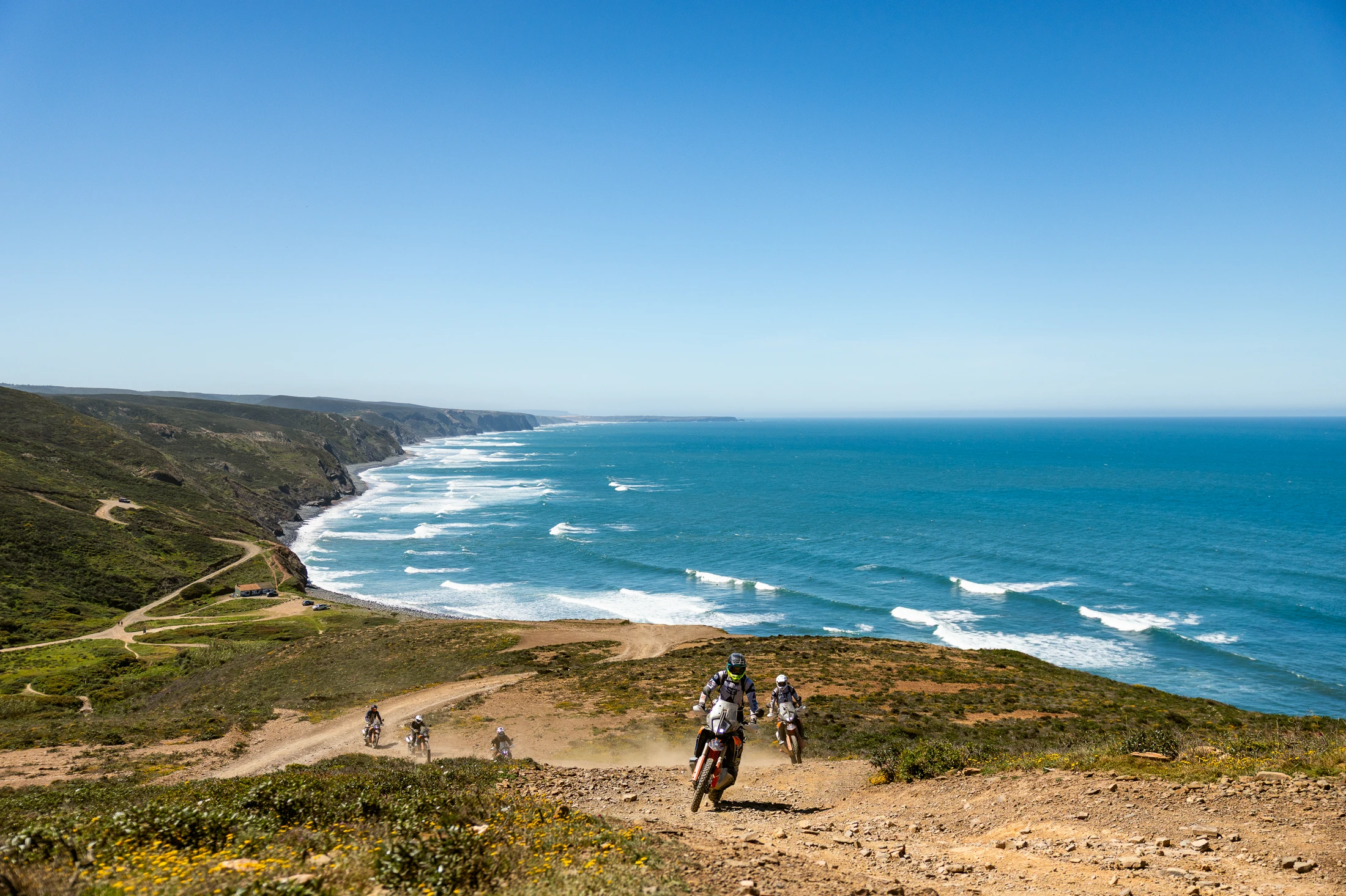 Riders on KTM adventure bikes on a dirt track above the Atlantic coast of the Algarve