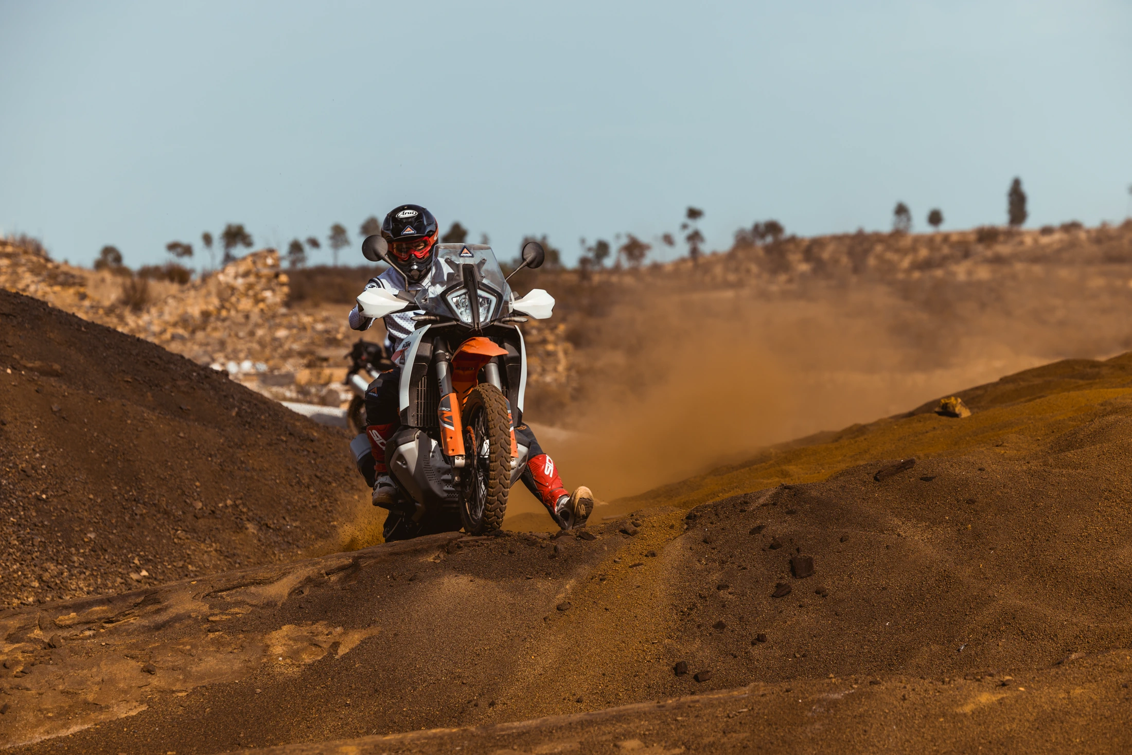 Rider on a KTM adventure bike sliding through red dirt on a hillside