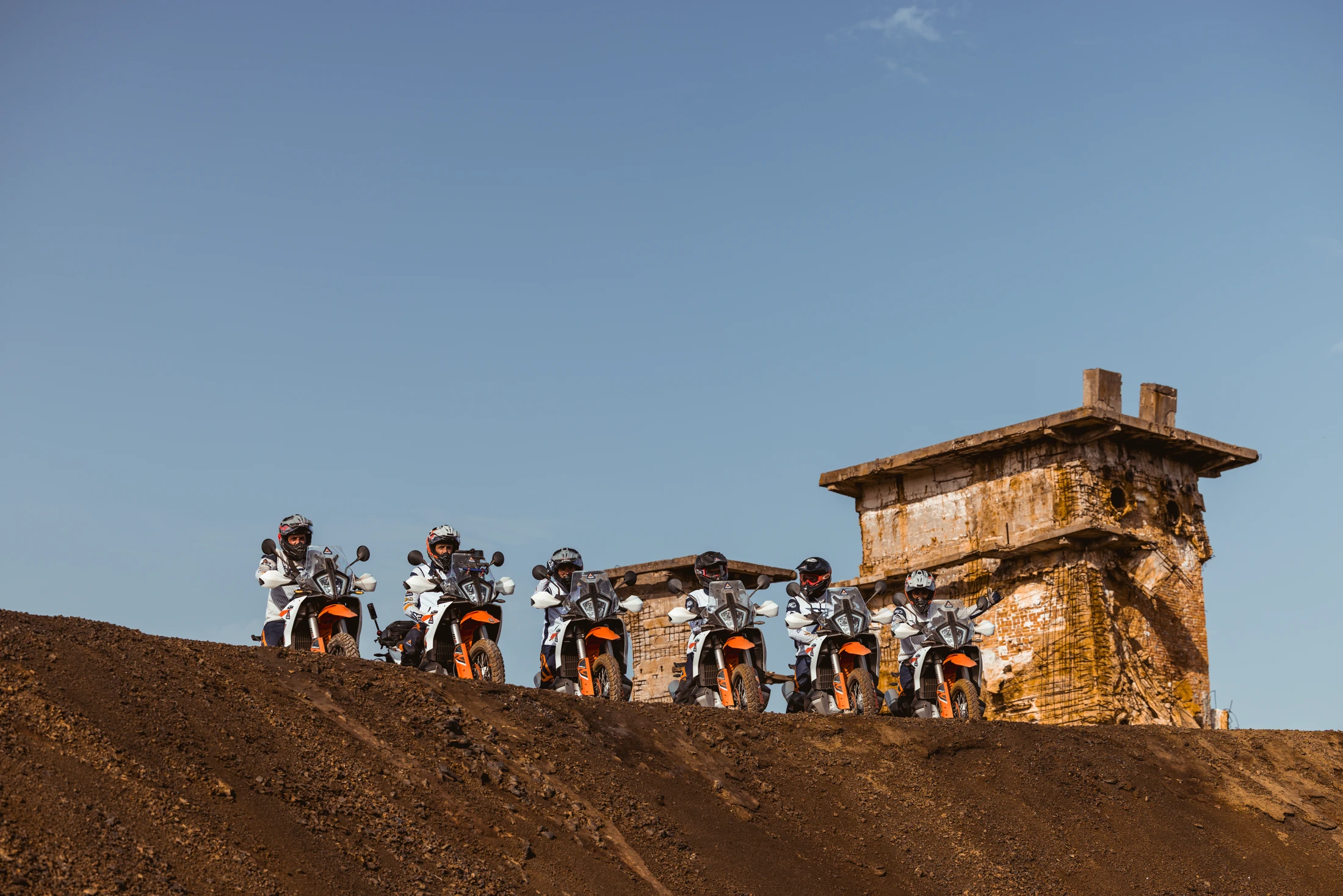 Group of riders on KTM adventure bikes lined up beside a stone ruin on a hilltop