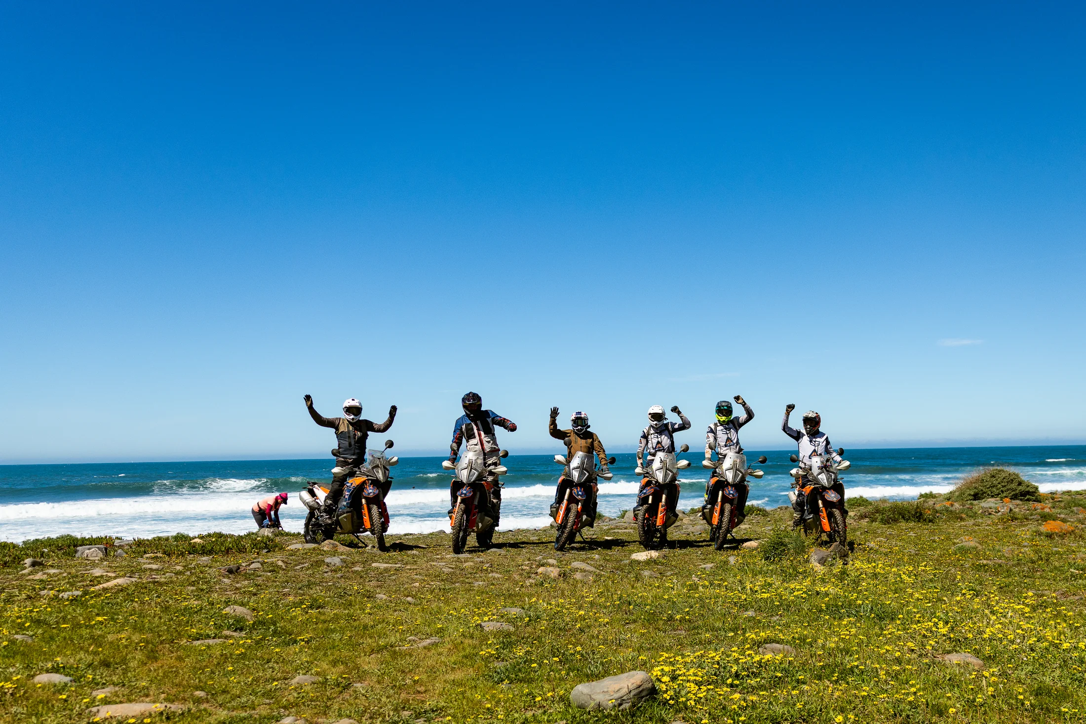 Group of riders cheering beside their KTM adventure bikes on the Atlantic coast of the Algarve