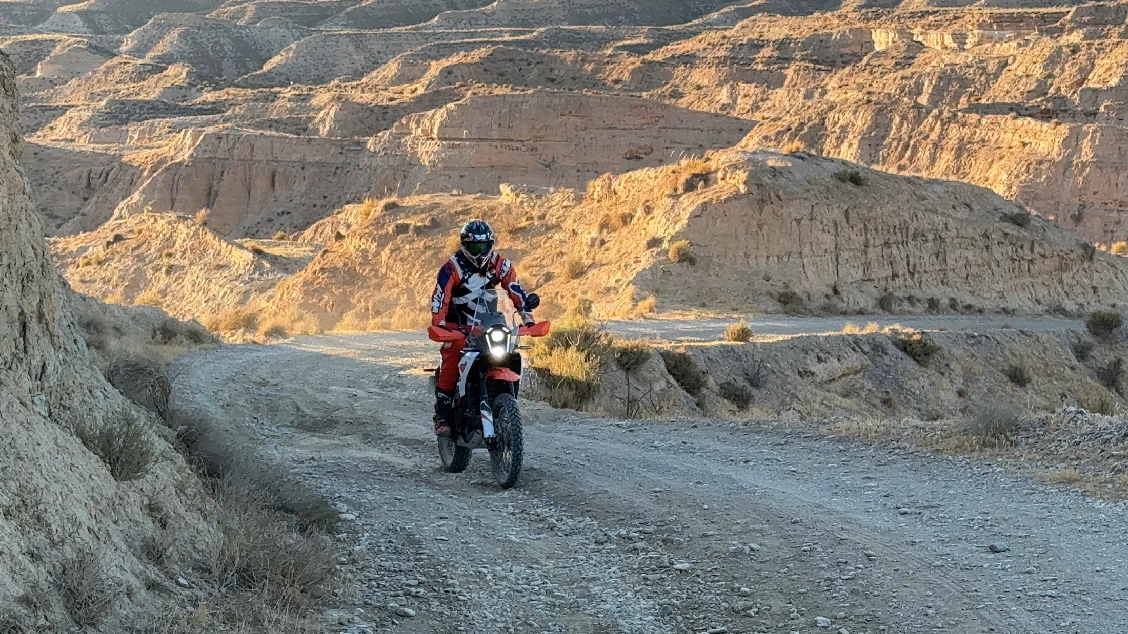 Rider on a KTM adventure bike descending a gravel road into the Gorafe desert canyons