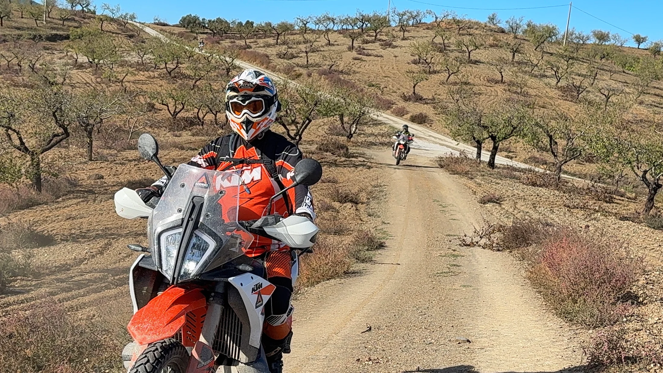 Rider on a KTM adventure bike on a dirt road through almond groves near Granada