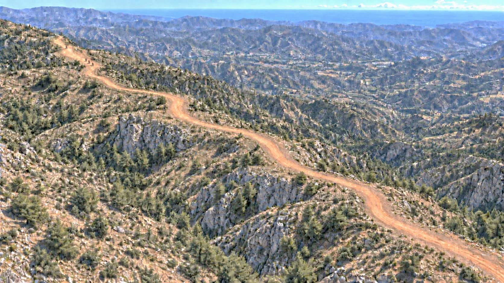 Aerial view of a dirt road winding across forested hills in Andalusia