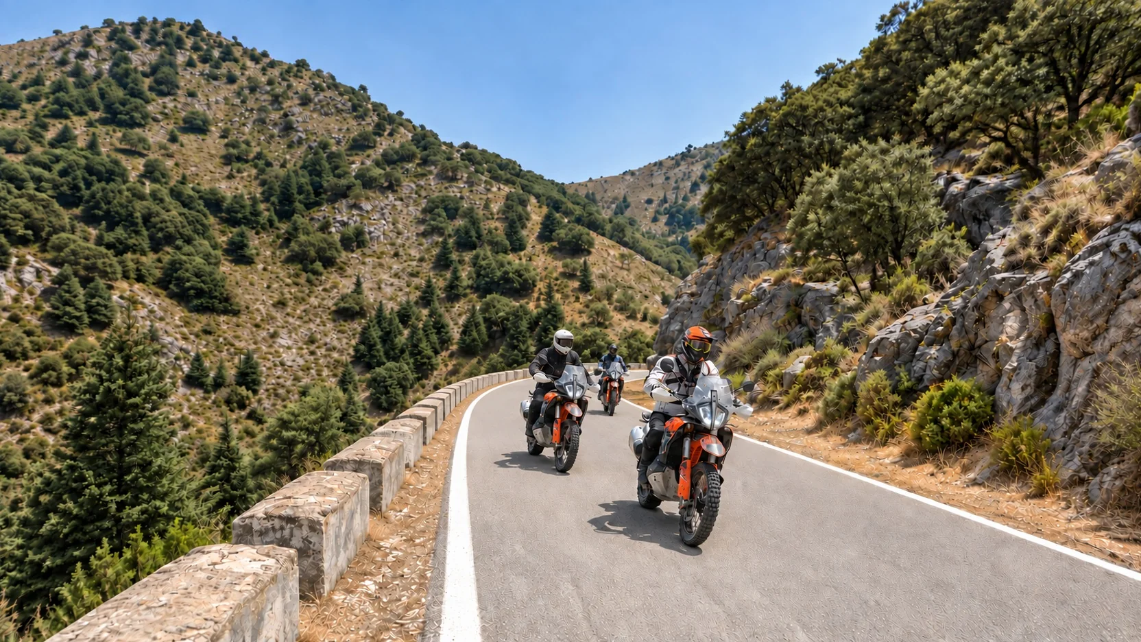 Riders on KTM adventure bikes on a mountain road with a stone wall in Andalusia