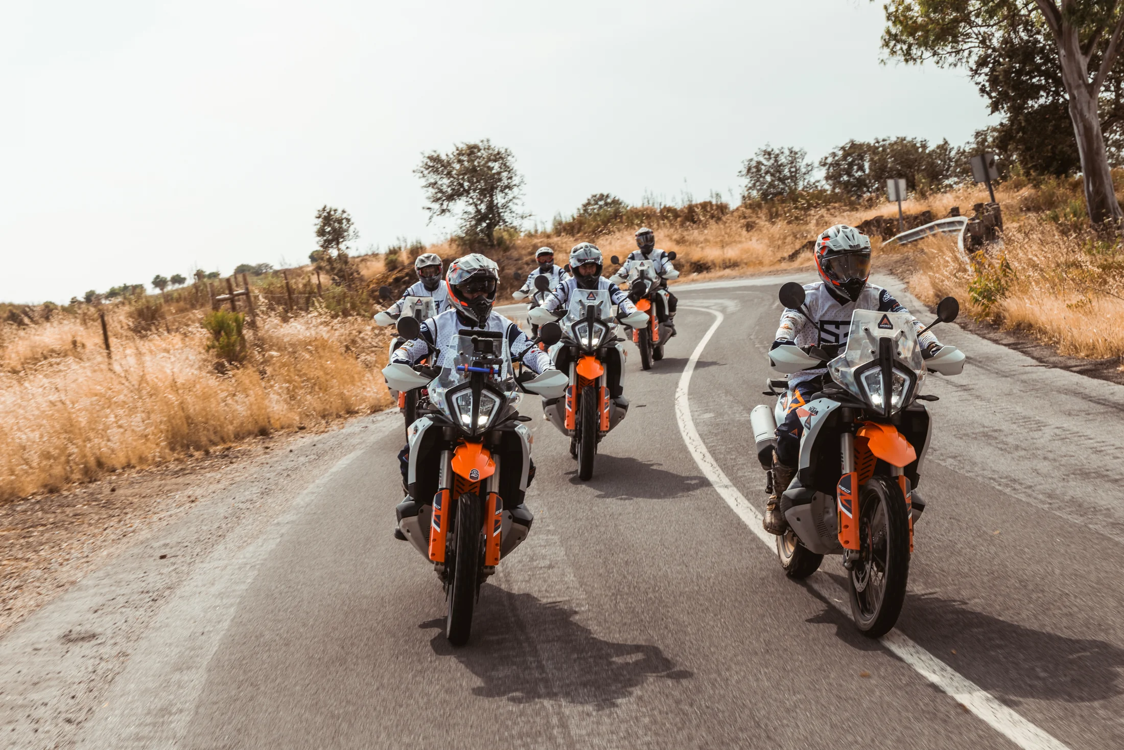 Group of riders on KTM adventure bikes on an asphalt bend through dry hills