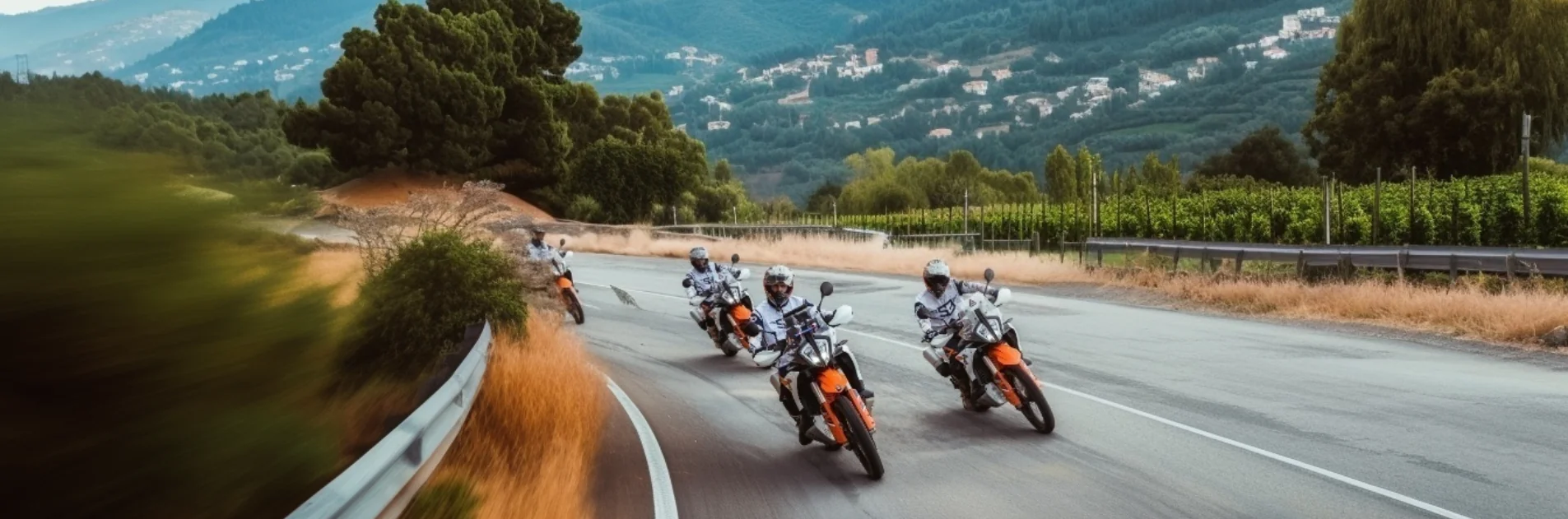 Riders on KTM adventure bikes on a fast road past vineyards and a white mountain village